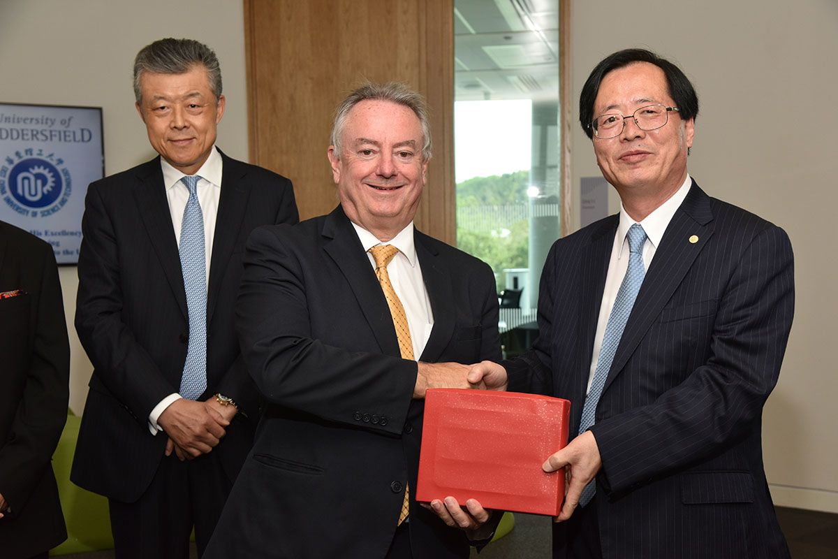 three men at the opening of the Confucius Institute, with two men shaking hands