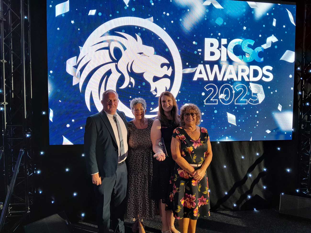 four of the cleaning team in front of an awards ceremony sign