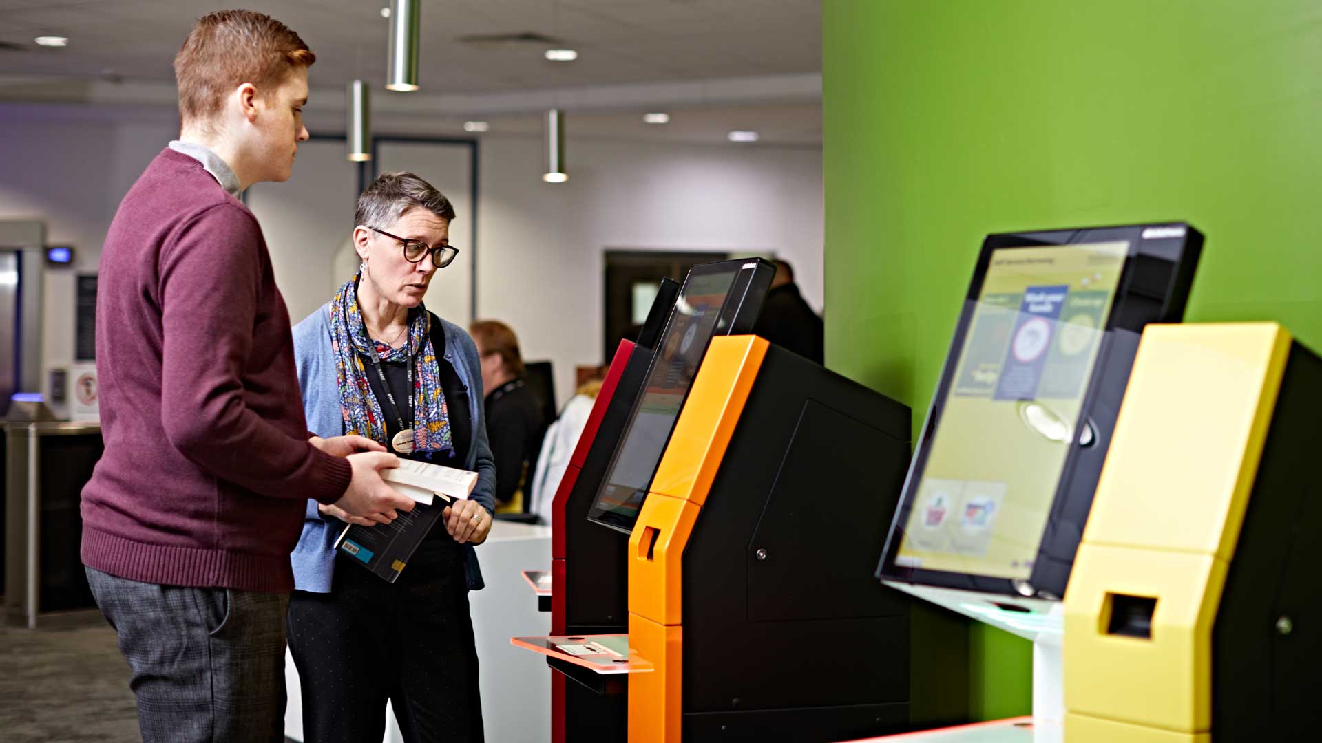 Student being assisted by a member of staff with the self-service machines in the University library