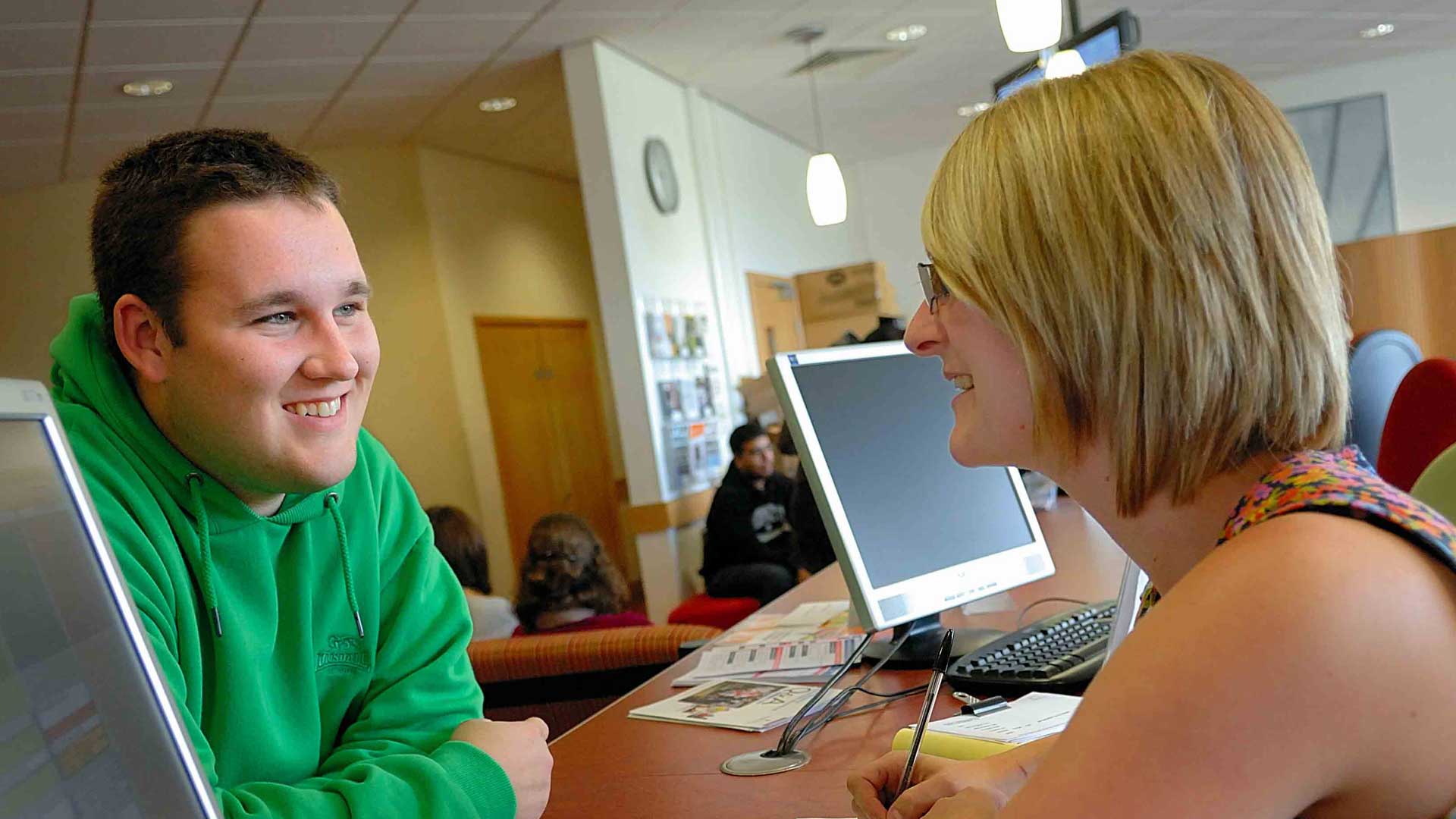 Picture of a student in green hoodie speaking with support staff