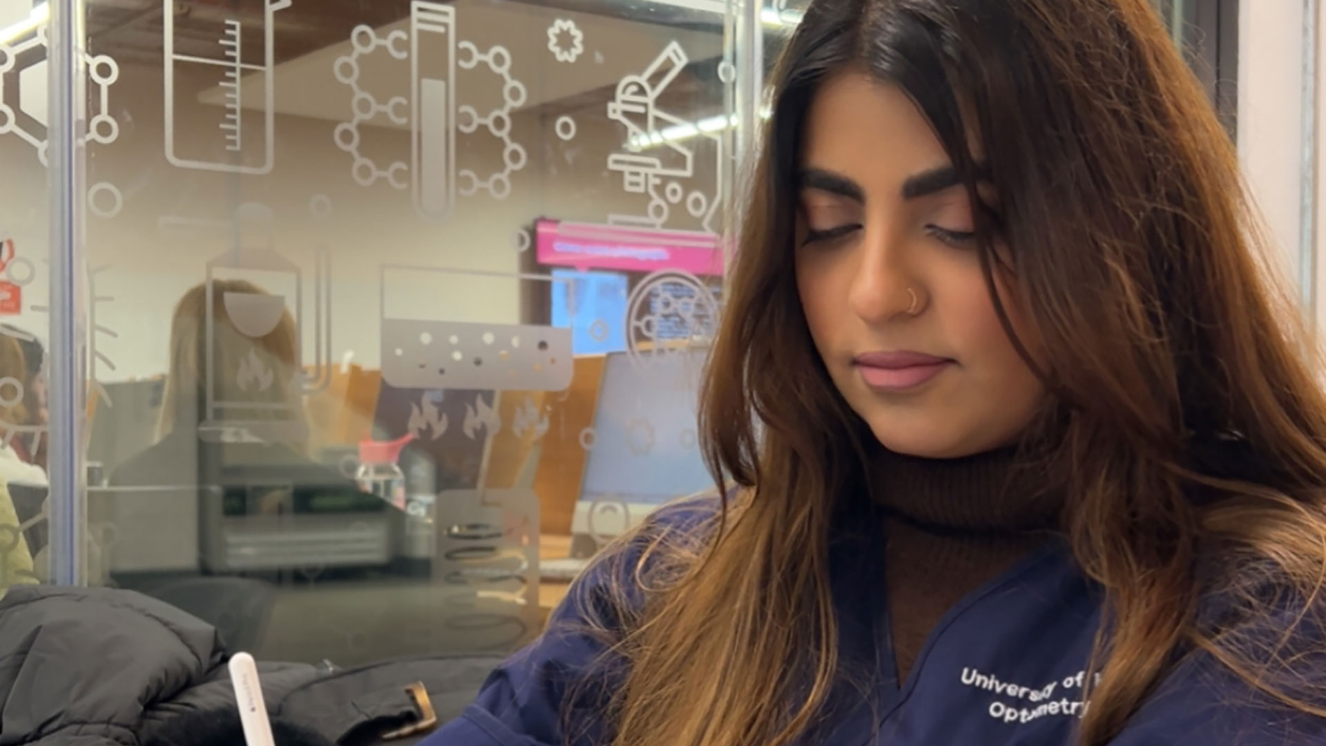 Ayesha in her Optometry uniform, writing notes on a tablet device.