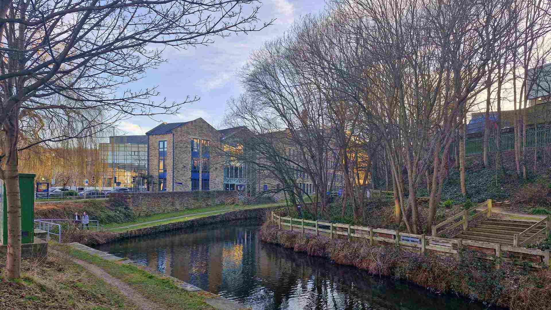 The canal which runs through the University campus, with campus mill style buildings in the background.