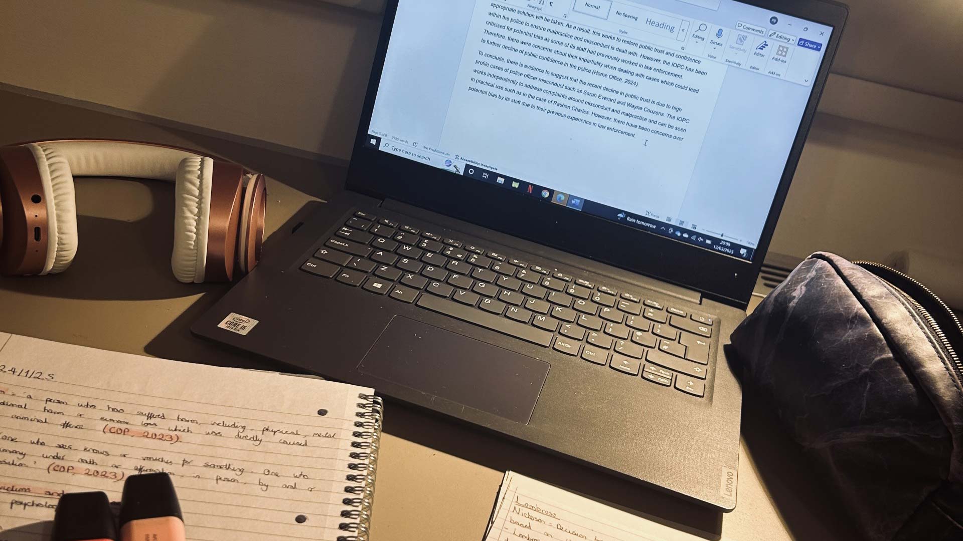 A laptop, notebook, pencil case and headphones on a desk.