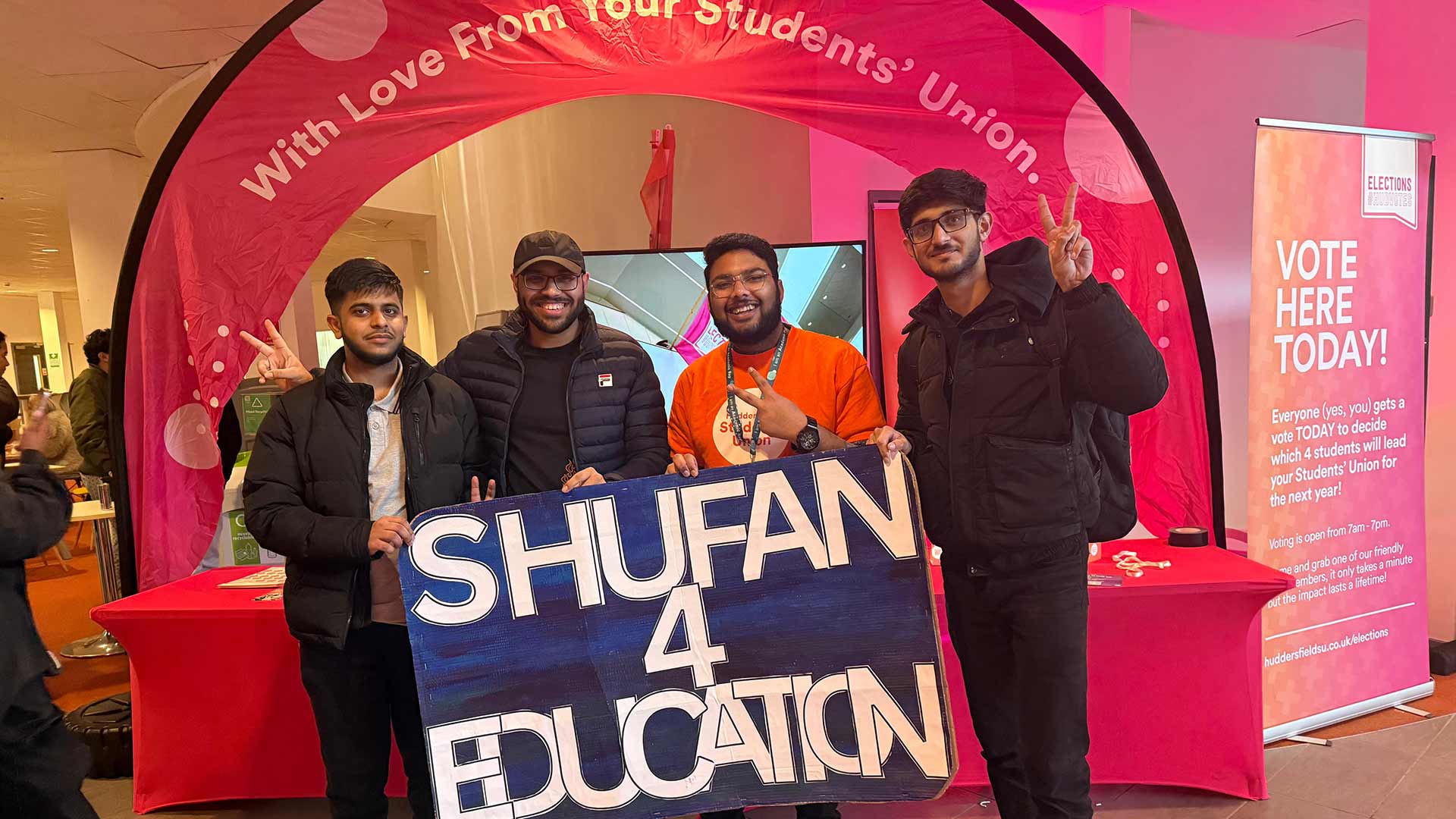 Shufan holding a large campaign banner for the Education Officer role with three students stood next to him.