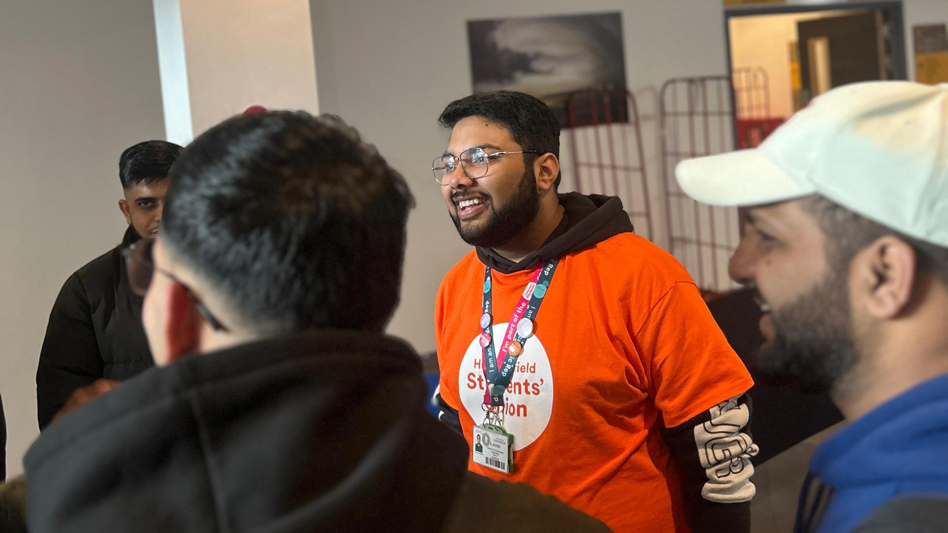 Shufan wearing an orange Students' Union t-shirt interacting with a small group of students.
