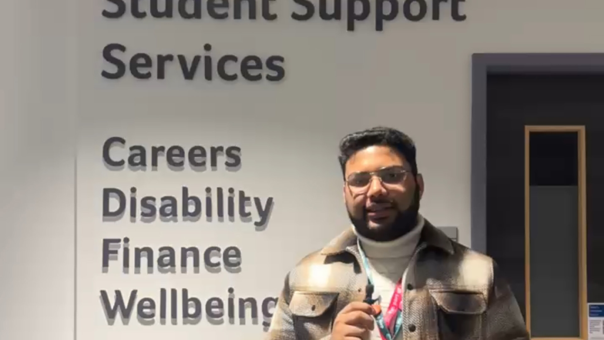 Shufan stood in front of a wall that lists the University's support services.