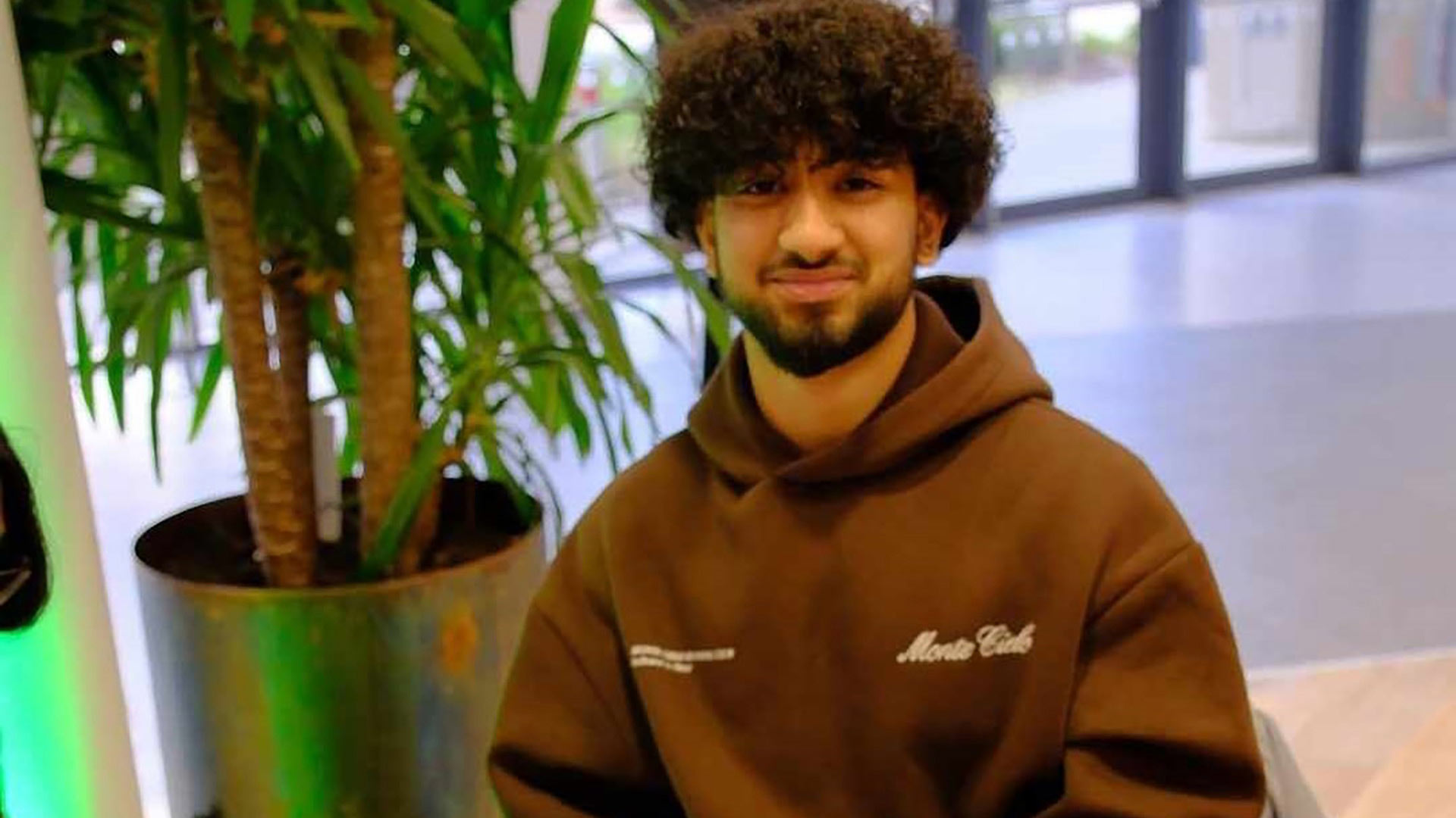 Syed sat a table, with a large plant behind him.