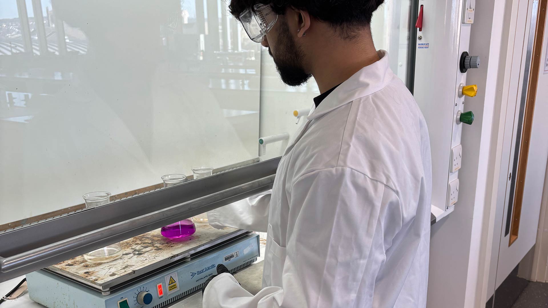Syed working in a science lab in a lab coat and goggles.