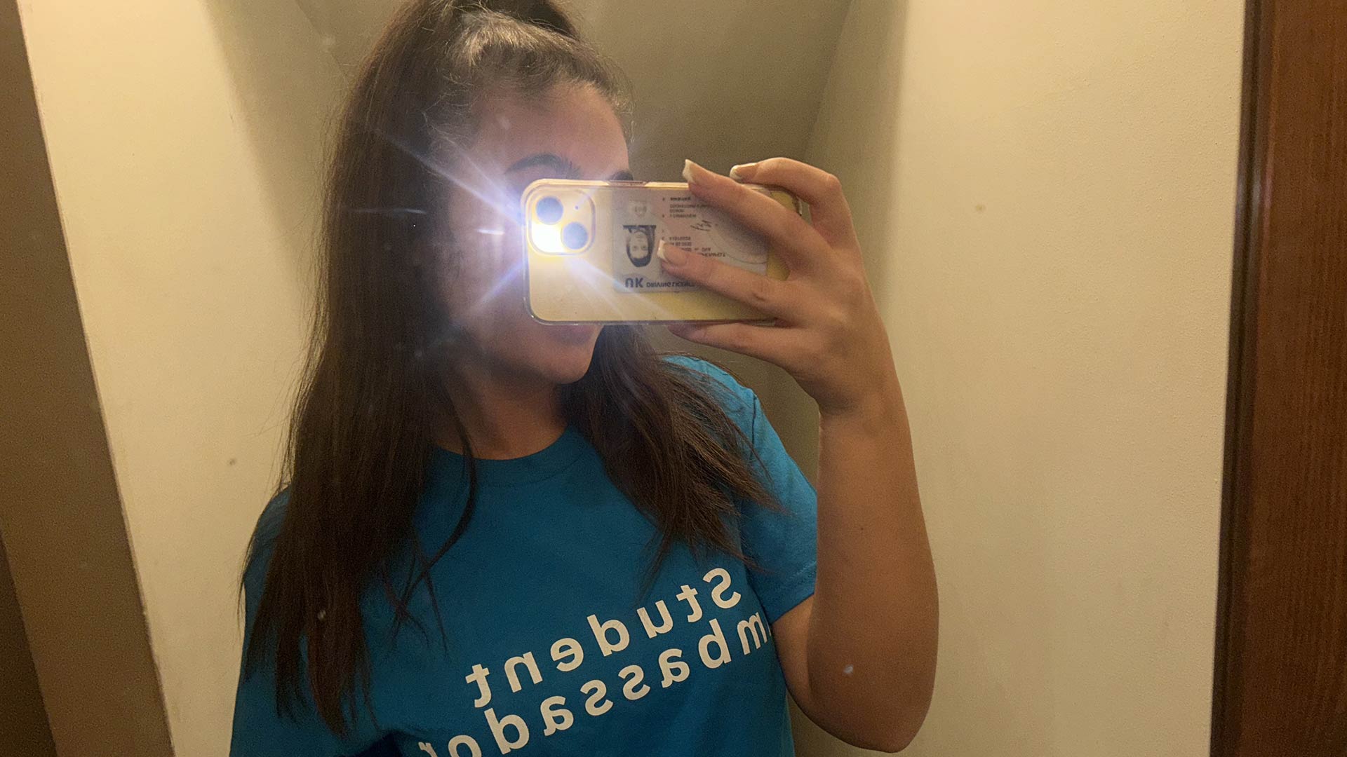 Tayler taking a selfie with the flash on, in her blue Student Ambassador t-shirt.