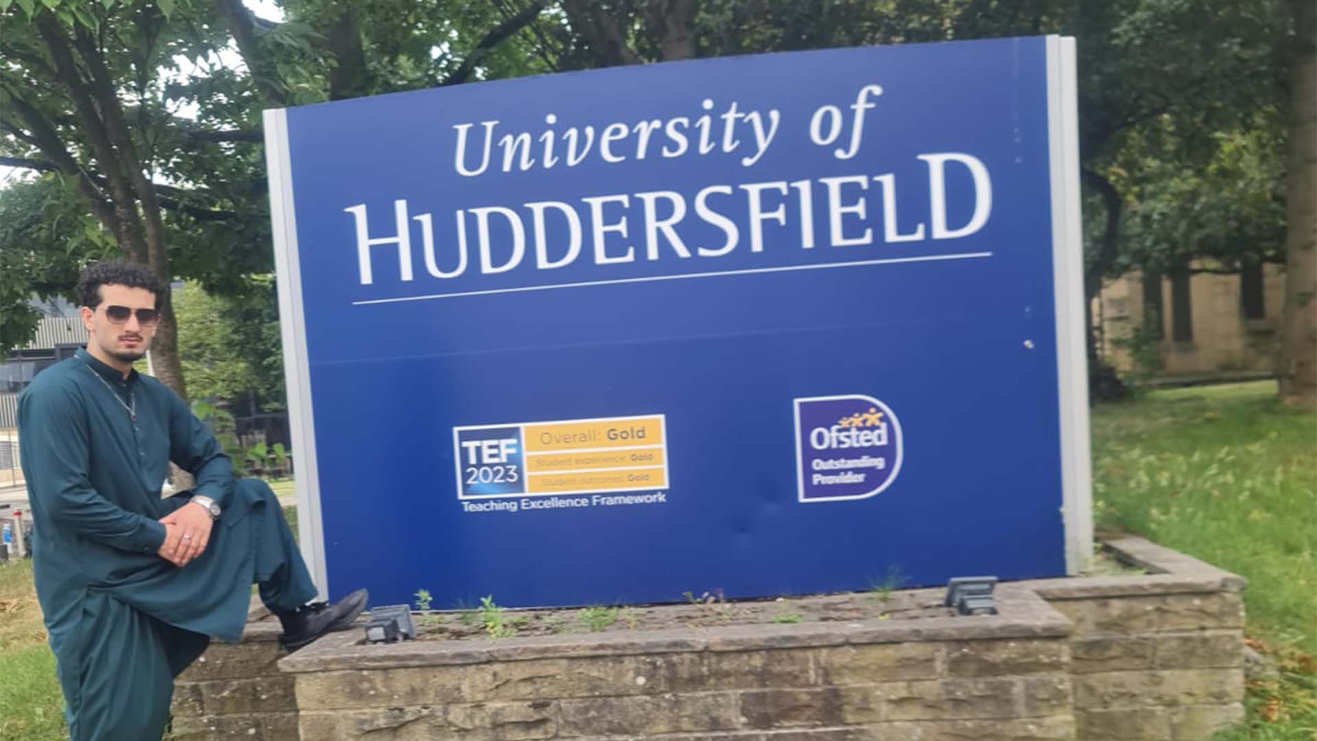 Saad Zahir standing by the University of Huddersfield sign on campus.