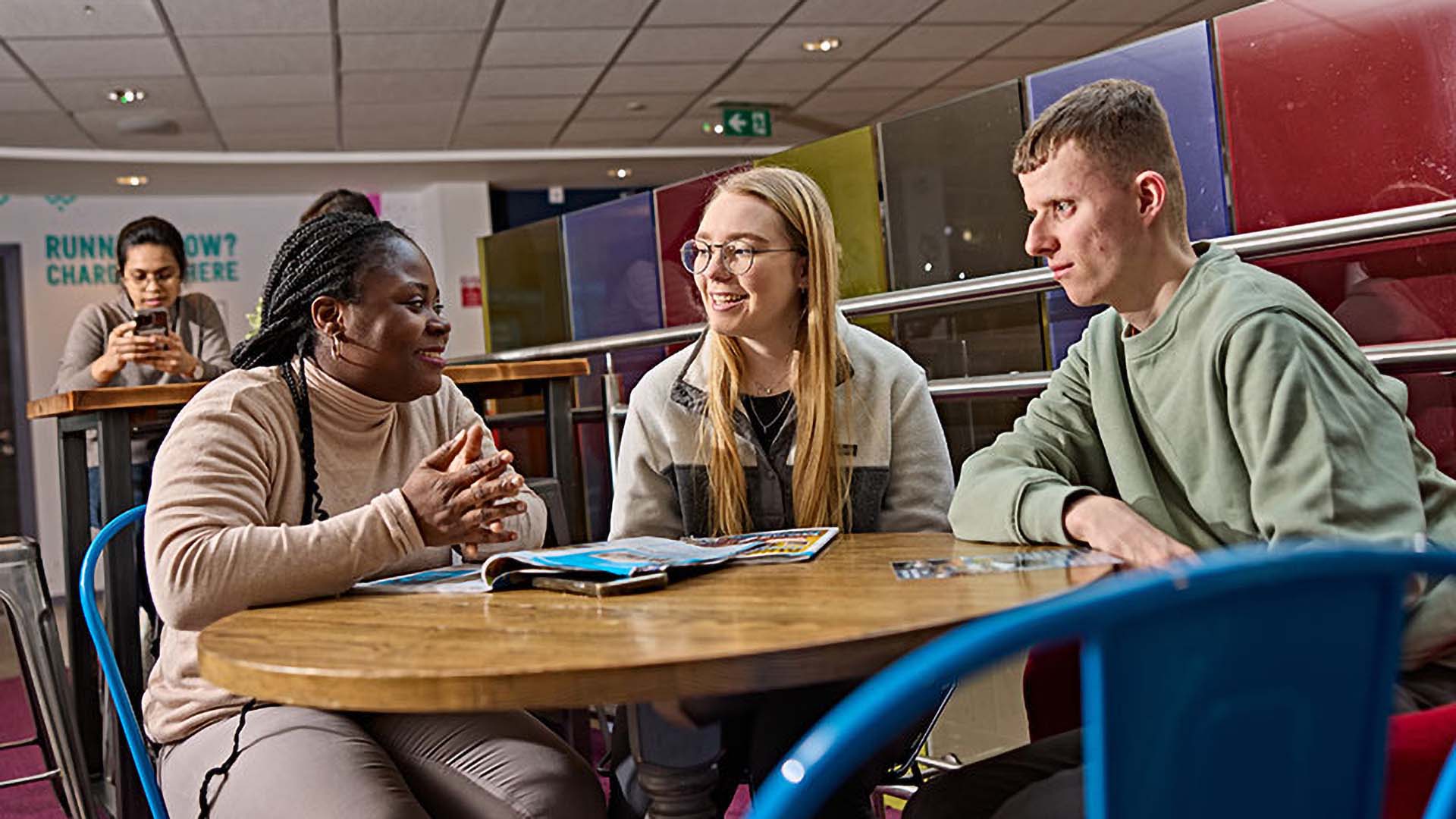 Three students sitting around a table in conversation.