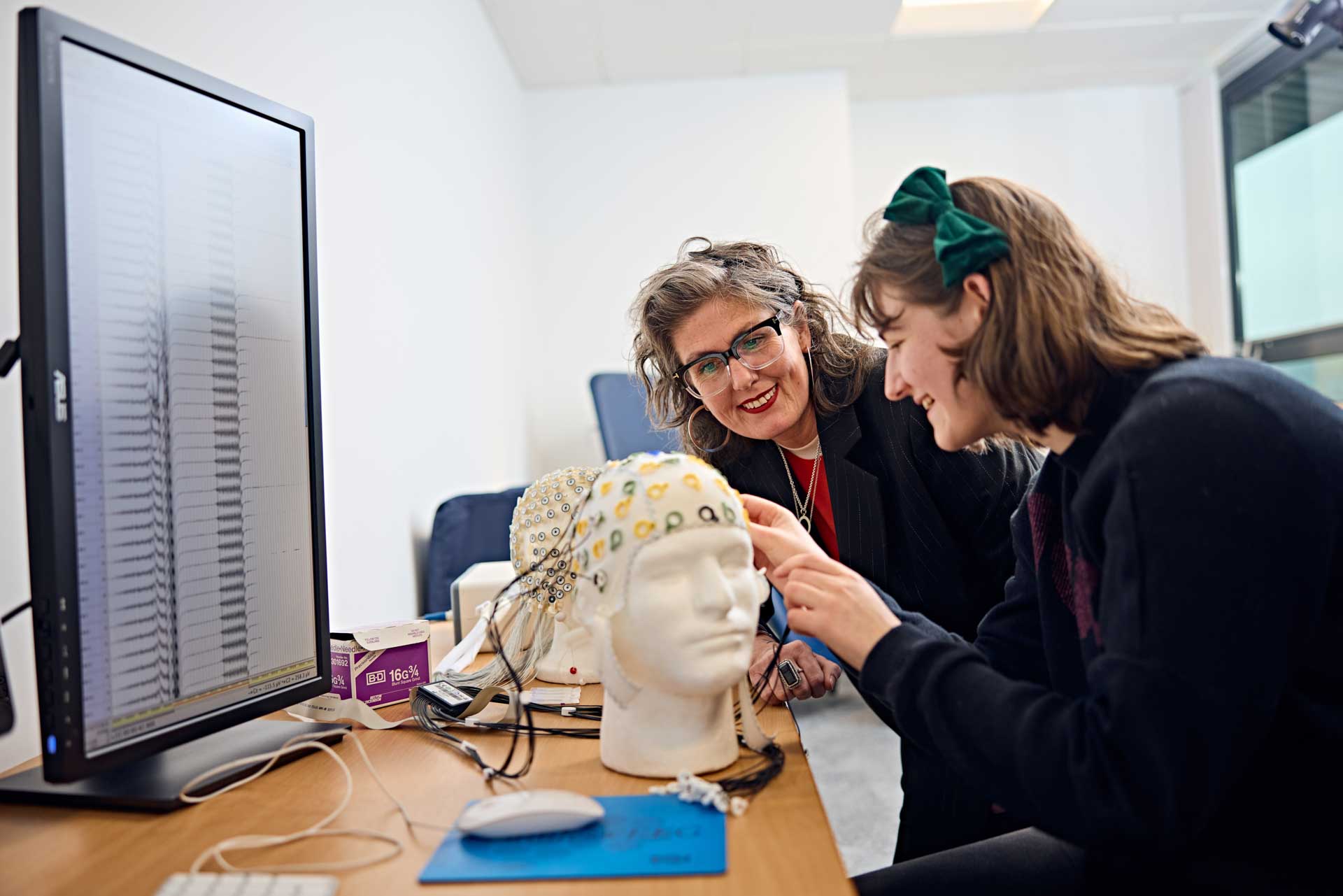 A psychology student and lecturer testing the measurements of an electroencephalography (EEG) cap before using it to measure electrical activity in the brain of a participant in their experiment.