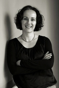 Georgina had brown bob length hair and is wearing a black top whilst smiling at the camera with her arms folded