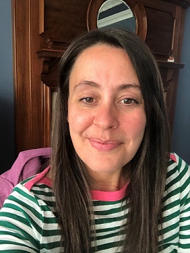 Josie has brown hair and is wearing a green and white striped top with a pink collar
