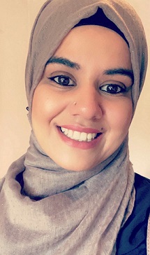 Maria is smiling at the camera and wears a grey headscarf