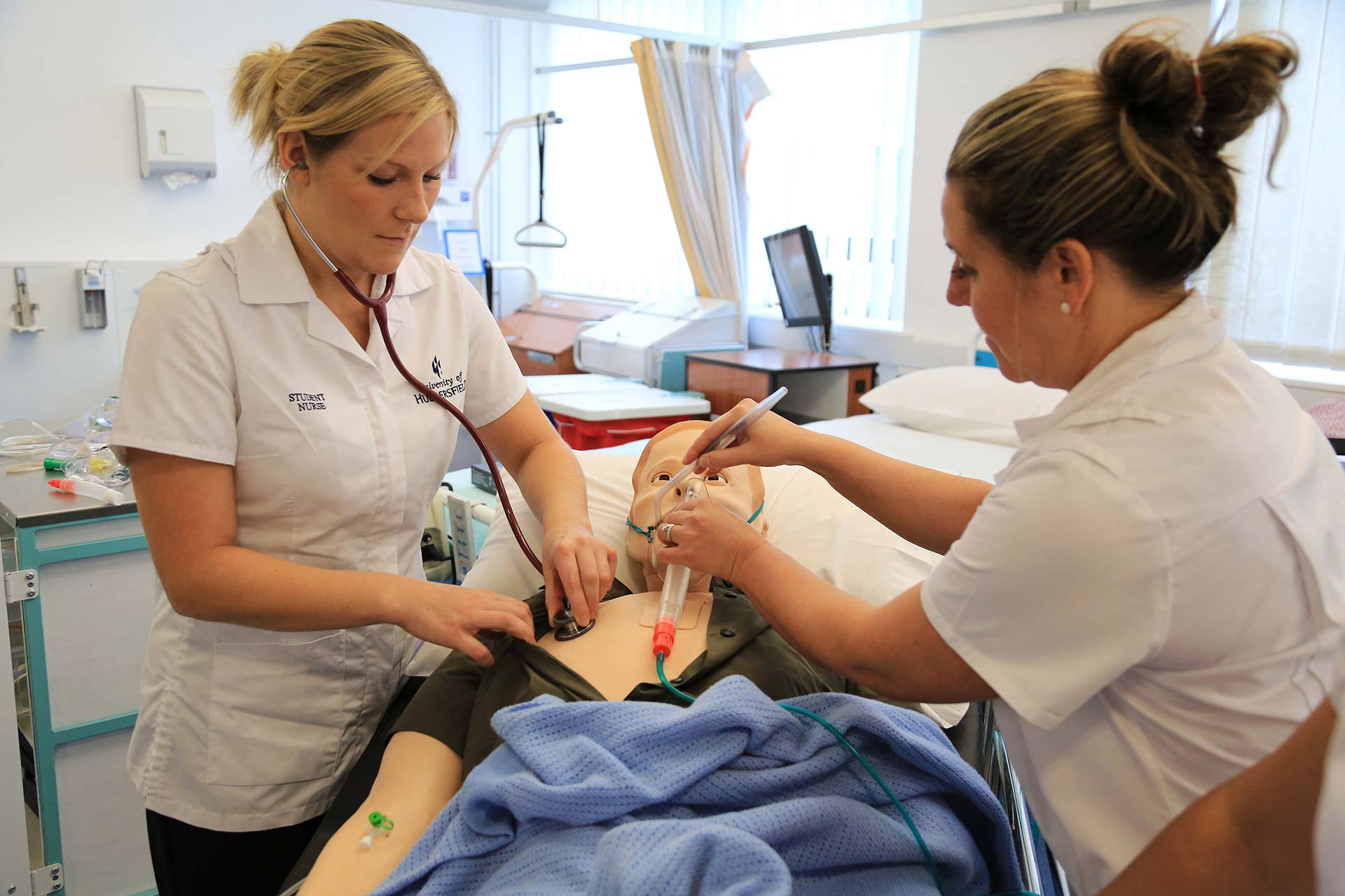 Nursing students applying breathing mask and stethoscope to an adult patient dummy