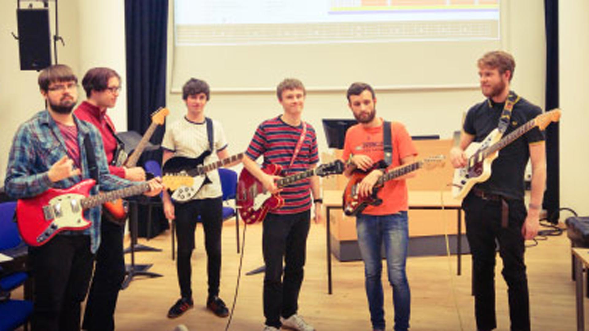 six men standing with guitars strapped onto them.